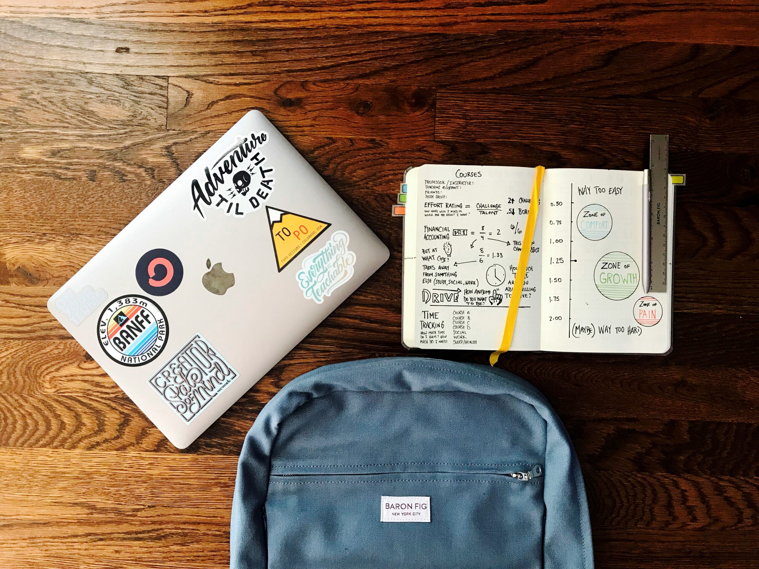 Laptop with study stickers, open research notebook, and backpack on a wooden desk